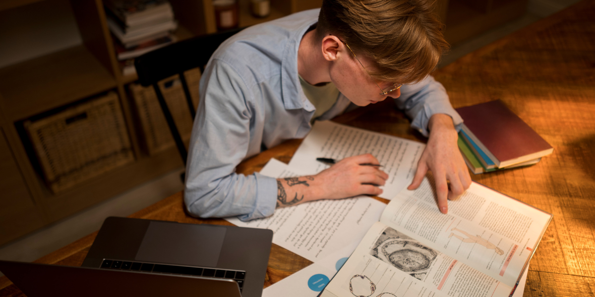 Student preparing for CA Foundation exam with books and laptop at study desk, focusing on notes and mock tests.